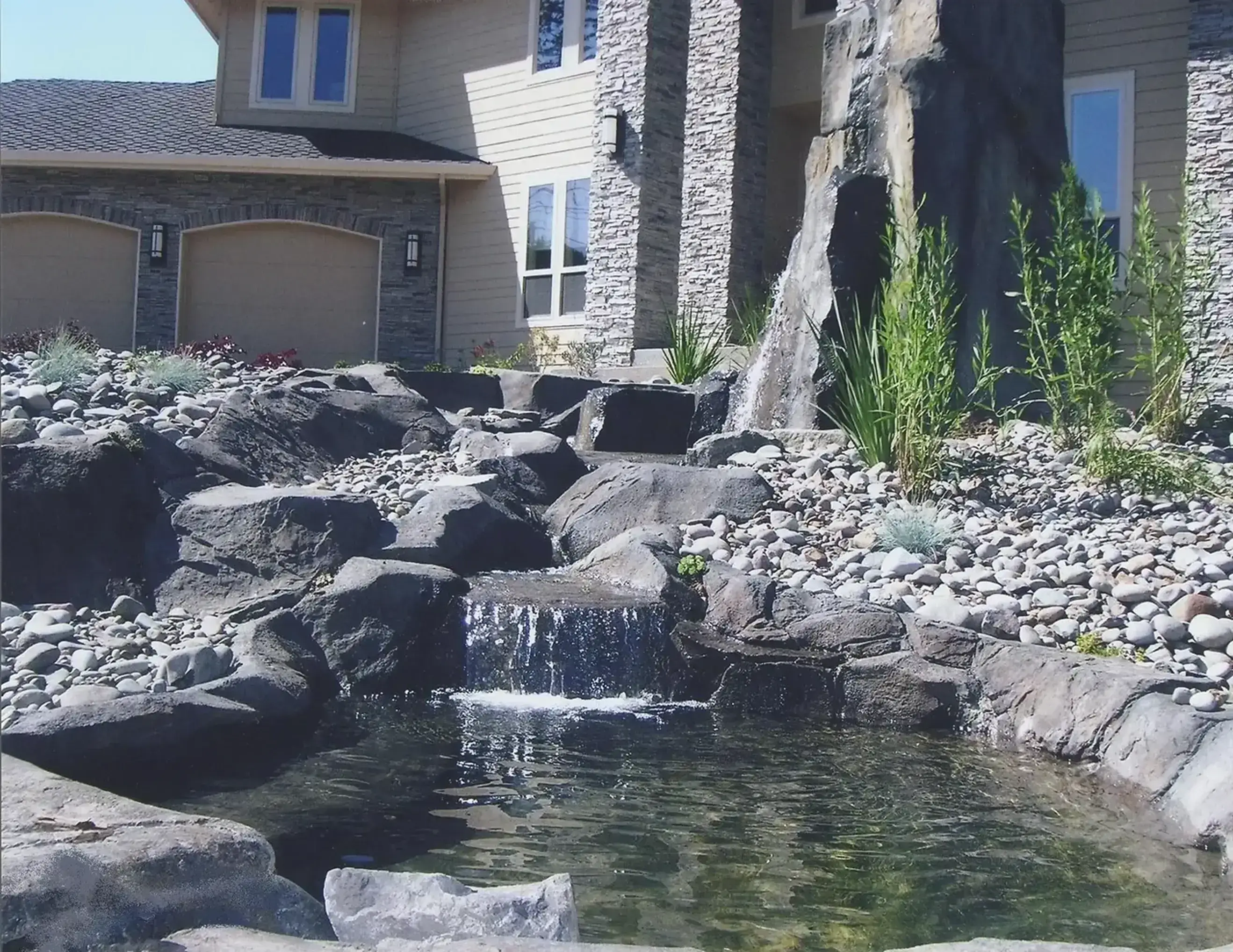 House exterior with stone waterfall and pond.